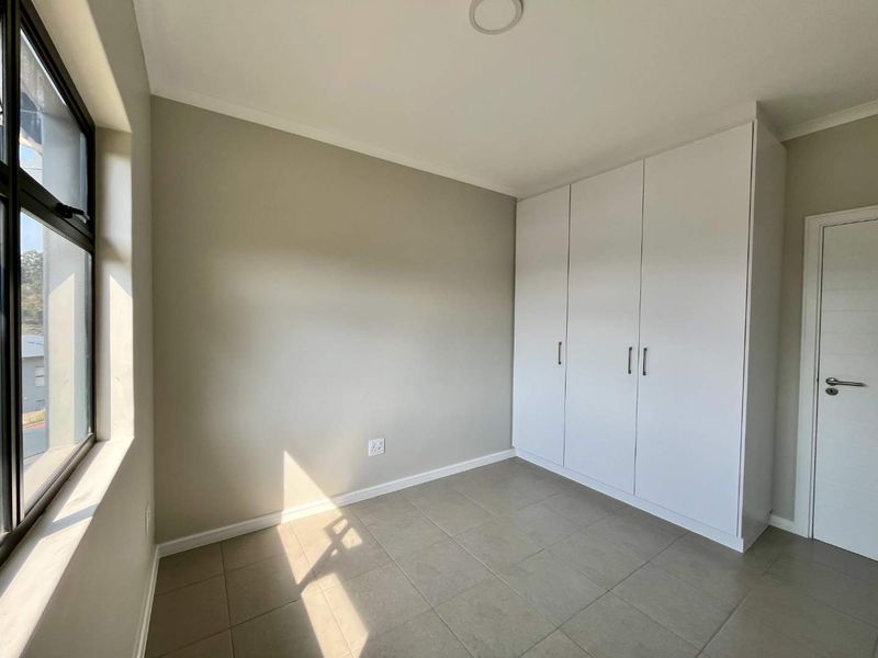A bright, empty bedroom featuring neutral wall tones, tiled flooring, and a modern white built-in wardrobe with clean lines.