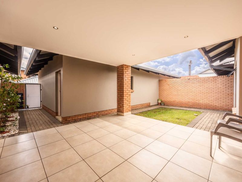 A spacious covered patio featuring tiled flooring, a brick support pillar, and direct access to a private paved courtyard and small garden area.