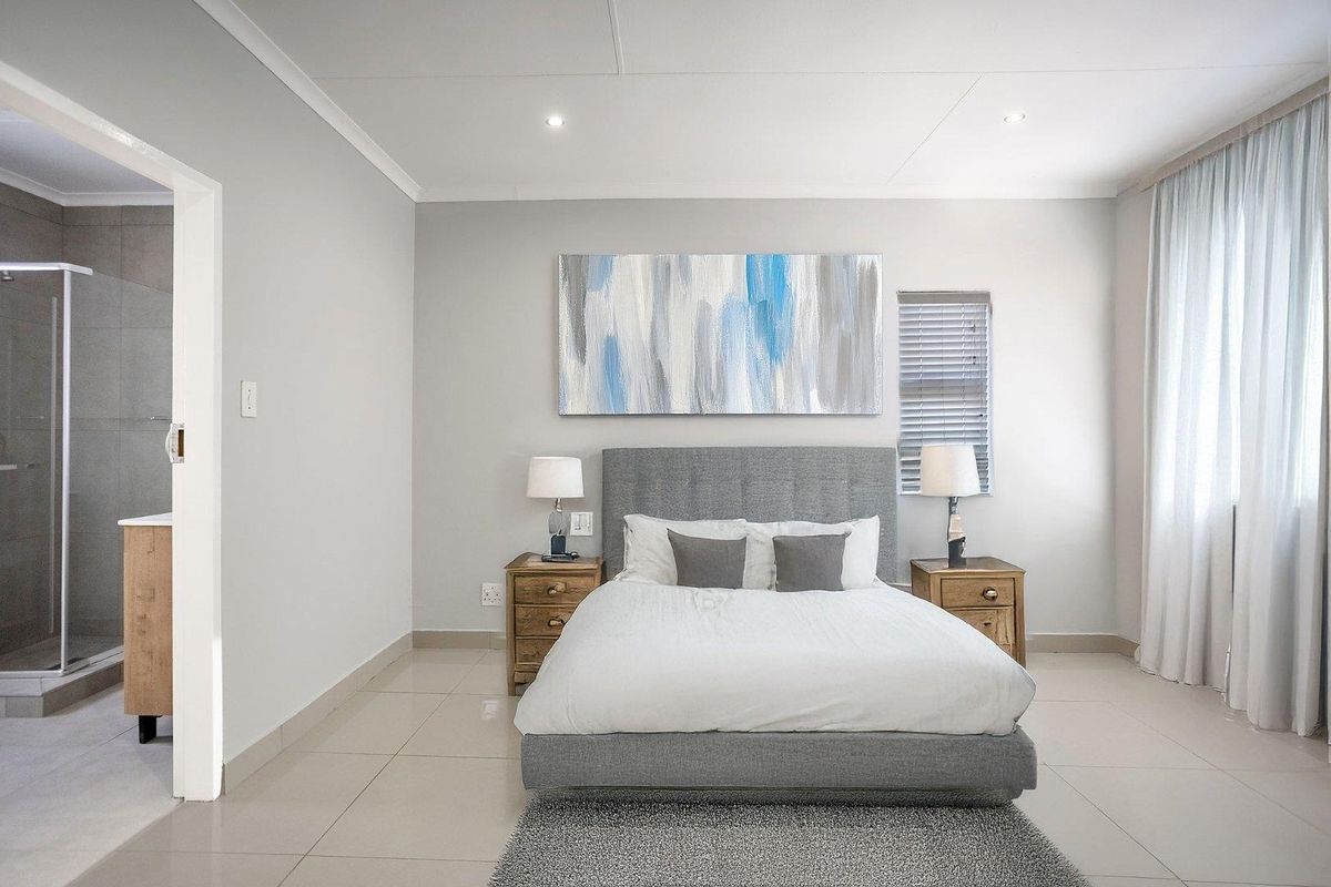 A well-maintained bedroom featuring neutral tiled flooring, recessed ceiling lighting, and an adjoining en-suite bathroom with a glass-enclosed shower.