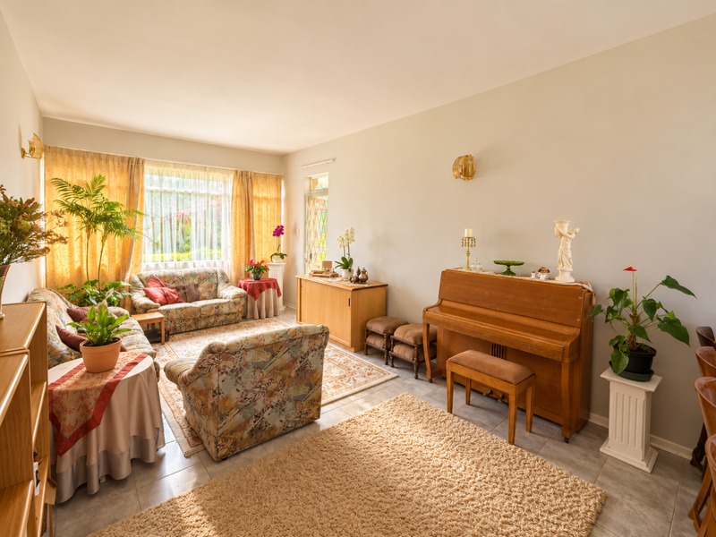 A spacious living room featuring tiled flooring, wall-mounted lighting, and a large window that allows for ample natural light.