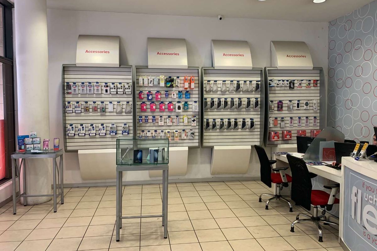 Retail store interior featuring wall-mounted slatwall display systems, recessed ceiling lighting, and a functional service counter area with tiled flooring.