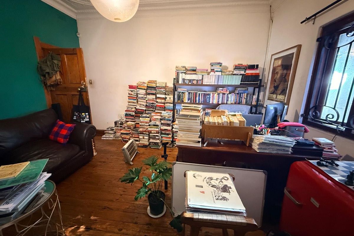 A living room featuring original timber flooring, decorative ceiling cornicing, and a security-grilled window, currently utilized as a home office and library space.