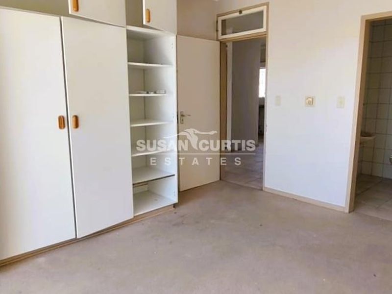 An empty bedroom featuring built-in cupboards and an attached en-suite bathroom with tiled flooring, offering a blank canvas for renovation.