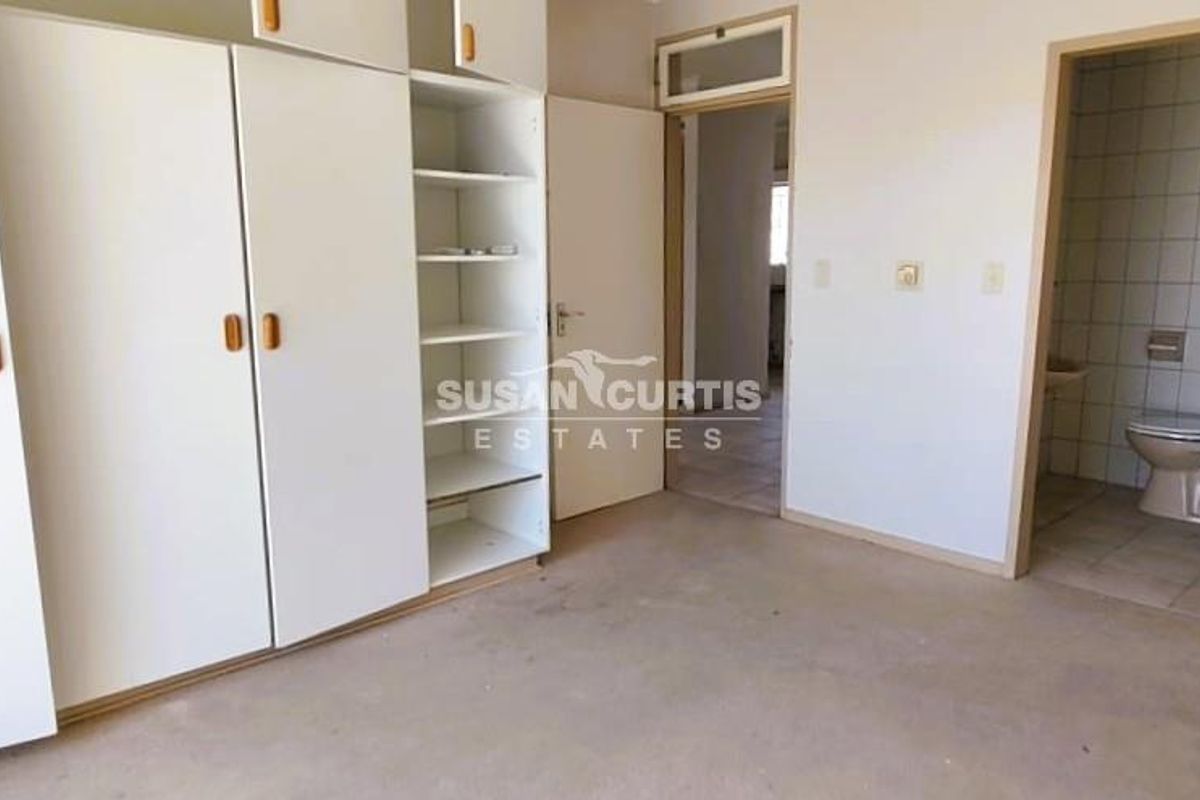 An empty bedroom featuring built-in cupboards and an attached en-suite bathroom with tiled flooring, offering a blank canvas for renovation.