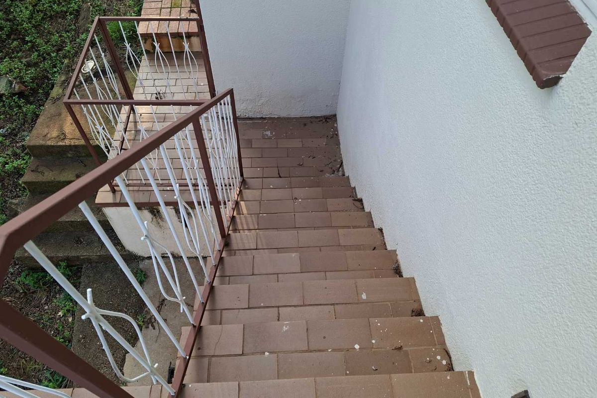Exterior staircase with tiled steps and a metal railing leading down to the garden area.