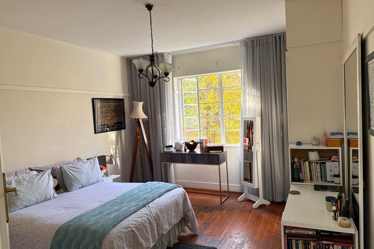 A bedroom featuring original hardwood flooring, a classic picture rail, and a large multi-pane window providing natural light and a pleasant garden view.