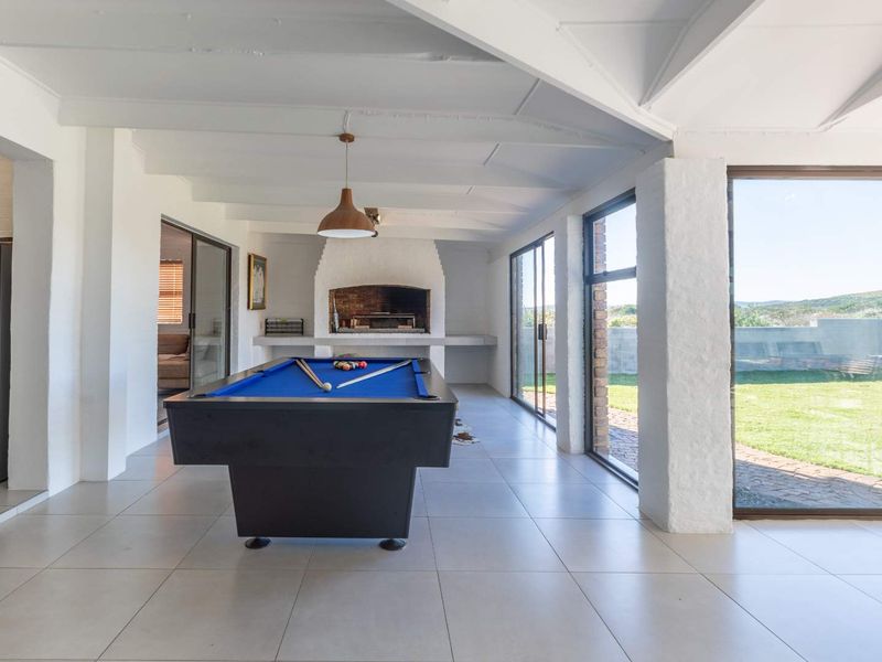 Spacious covered patio featuring tiled flooring, exposed beam ceilings, and a built-in braai, with large sliding glass doors opening to the garden.
