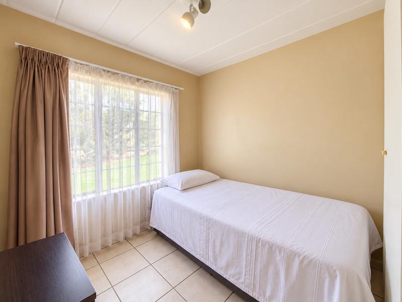 A functional bedroom featuring tiled flooring, a built-in cupboard, and natural light through a large window.