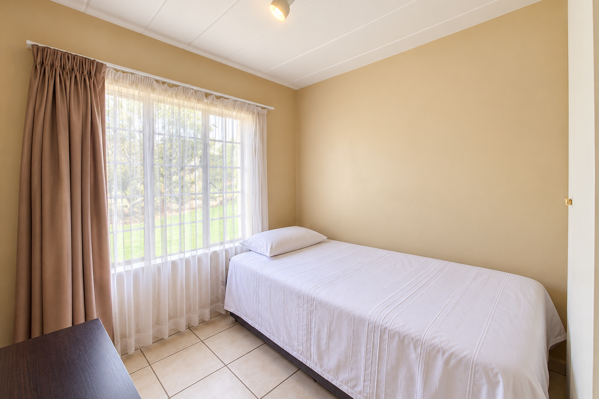 A functional bedroom featuring tiled flooring, a built-in cupboard, and natural light through a large window.