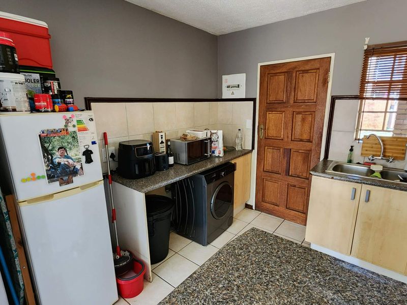 Functional scullery area featuring built-in cabinetry, granite countertops, a stainless steel sink, and dedicated space for laundry appliances.