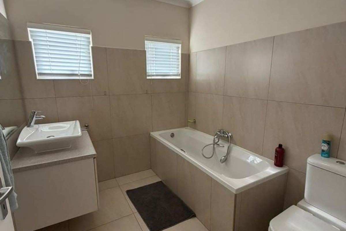 A clean, modern bathroom featuring a built-in vanity with a vessel sink, a bathtub, and neutral floor-to-ceiling wall tiling.