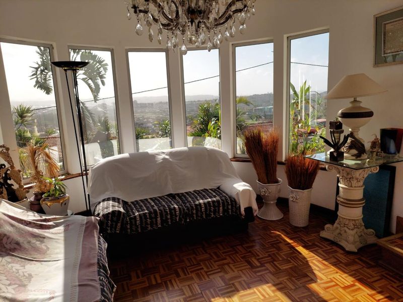 A bright living room featuring classic parquet flooring, a decorative crystal chandelier, and expansive bay windows offering panoramic views.