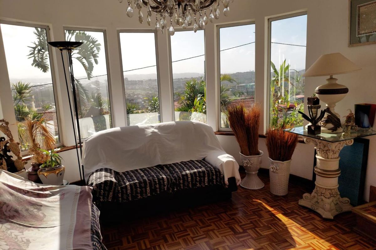 A bright living room featuring classic parquet flooring, a decorative crystal chandelier, and expansive bay windows offering panoramic views.