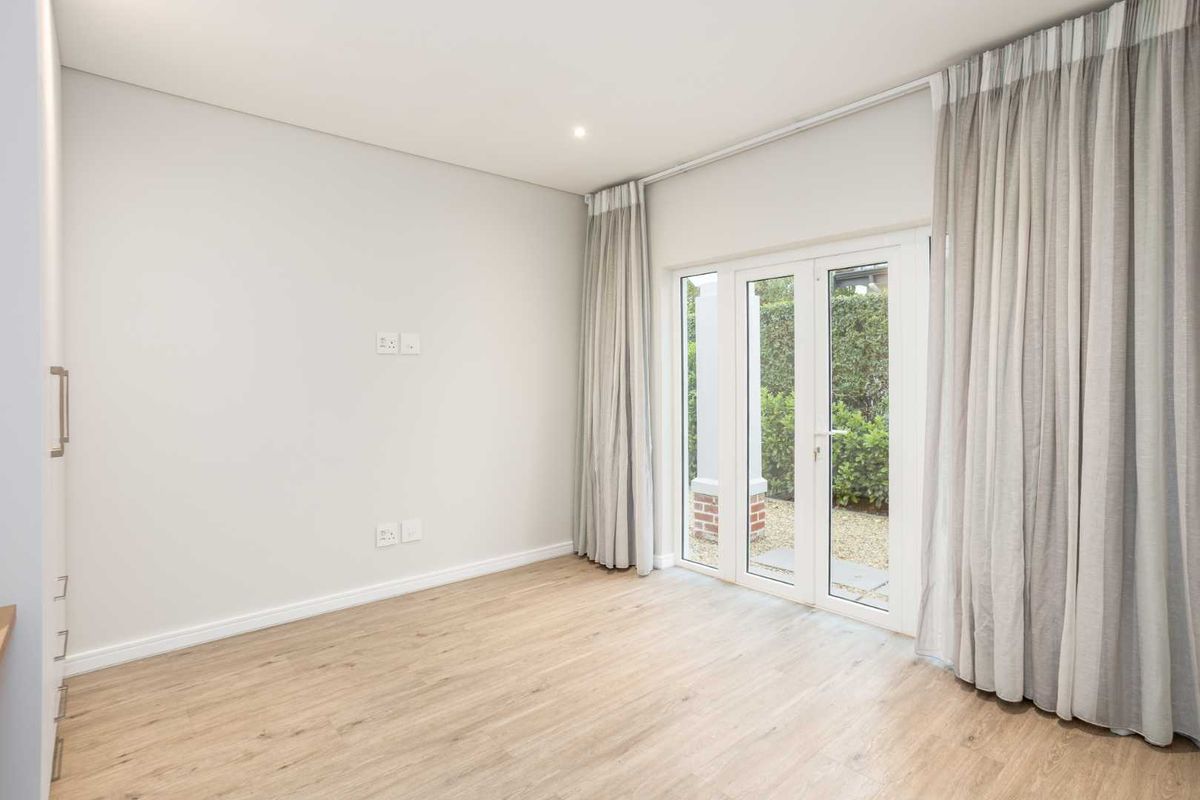 A bright, modern bedroom featuring light laminate flooring, built-in cupboards, and glass french doors providing direct access to the garden.