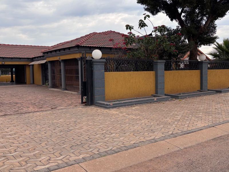 Front exterior view of the property featuring a paved driveway, secure perimeter wall with wrought iron fencing, and a tiled roof structure.