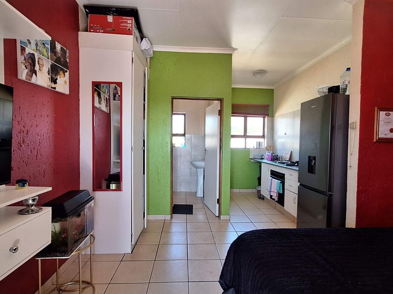 Open-plan living area featuring a compact kitchen with built-in cabinetry and oven, tiled flooring, and direct access to an adjoining bathroom.