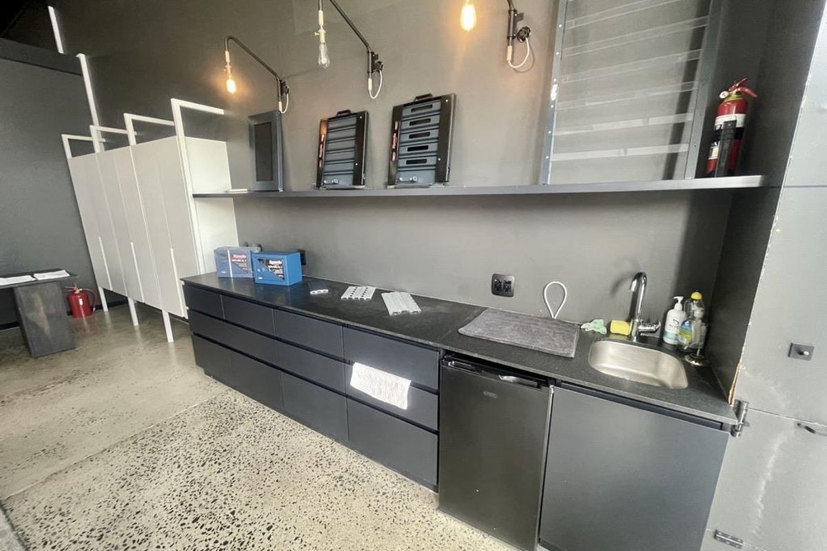 Modern kitchenette area featuring dark cabinetry, integrated sink, polished concrete flooring, and industrial-style wall-mounted lighting fixtures.