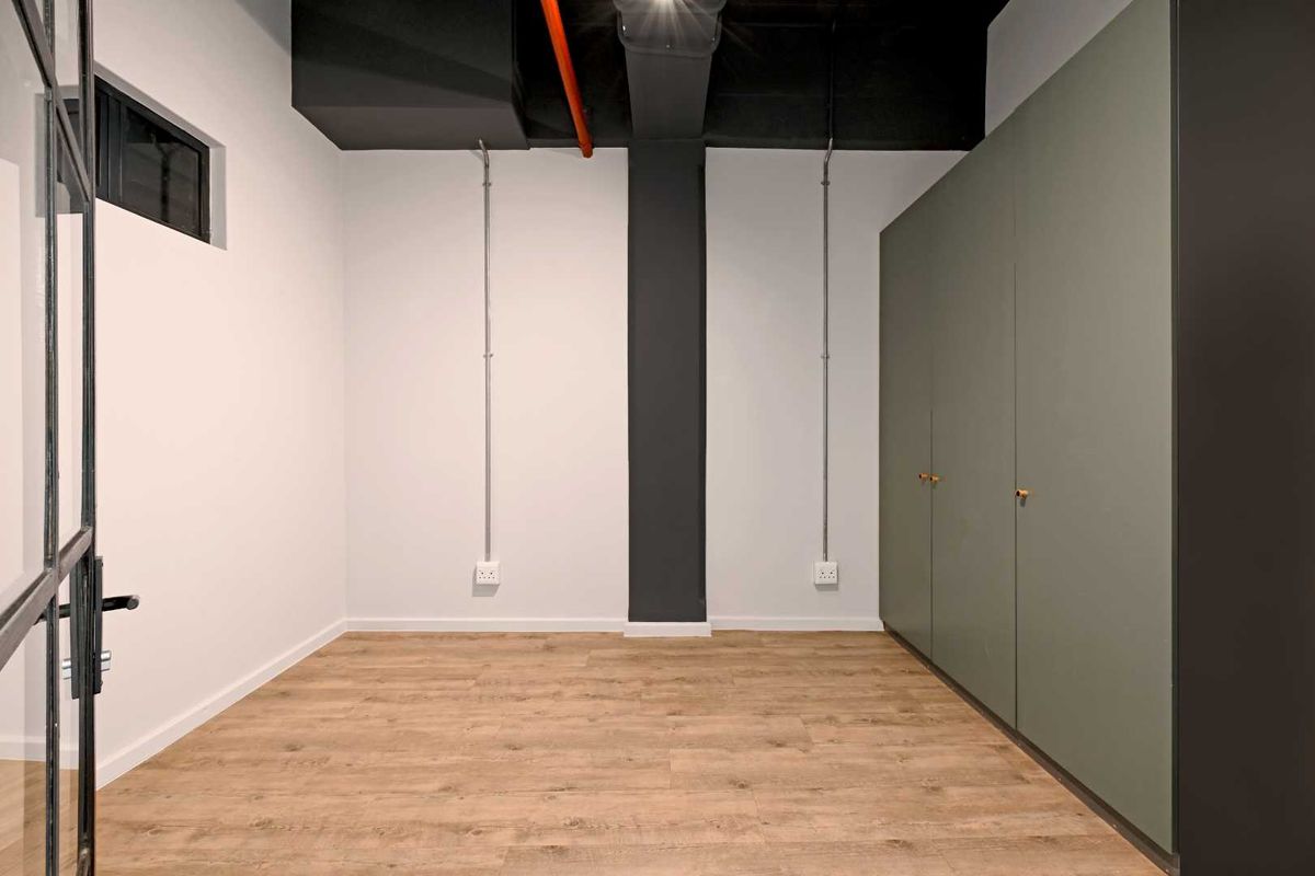 A modern, empty bedroom featuring laminate flooring, built-in cupboards, and an industrial-style exposed ceiling and conduit design.