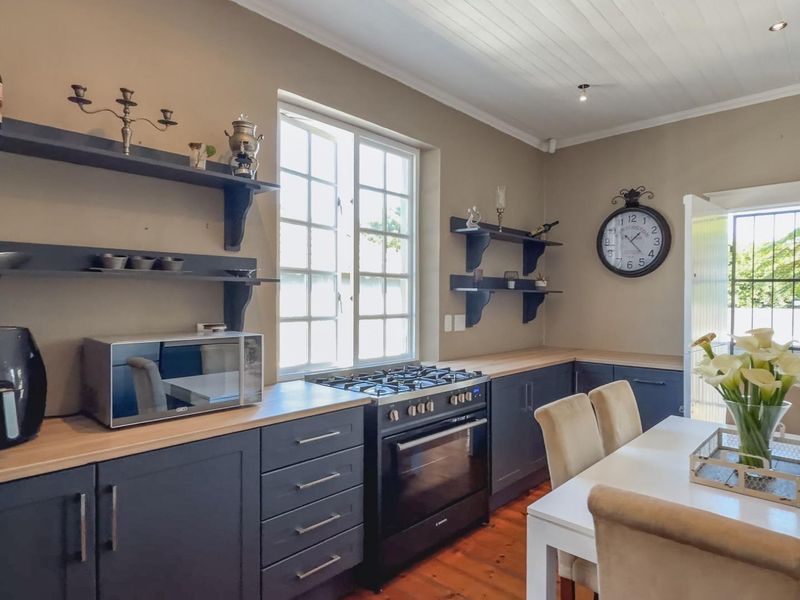 A well-maintained kitchen featuring dark cabinetry, wooden countertops, a gas stove with oven, and open shelving, complemented by warm timber flooring.