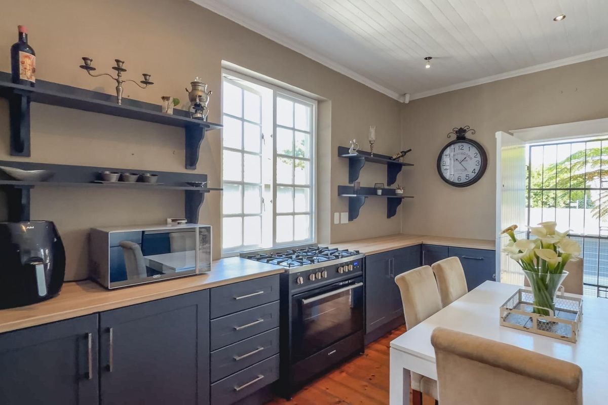A well-maintained kitchen featuring dark cabinetry, wooden countertops, a gas stove with oven, and open shelving, complemented by warm timber flooring.