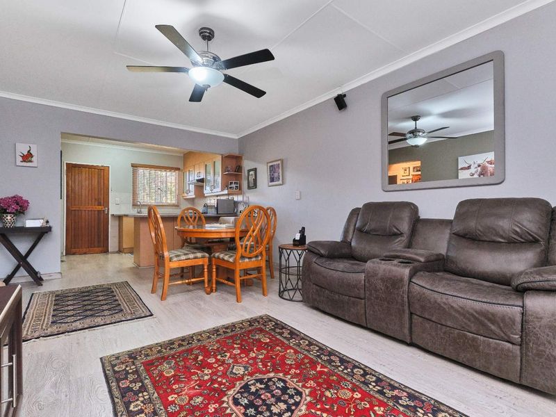 Open-plan living and dining area featuring laminate flooring, a ceiling fan, and an adjoining kitchen with wooden cabinetry.
