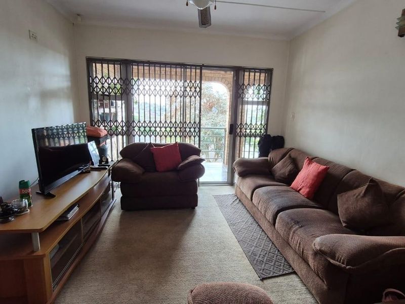 A living room featuring a sliding glass door with security gate, ceiling fan, and wall lighting, providing access to an outdoor area.