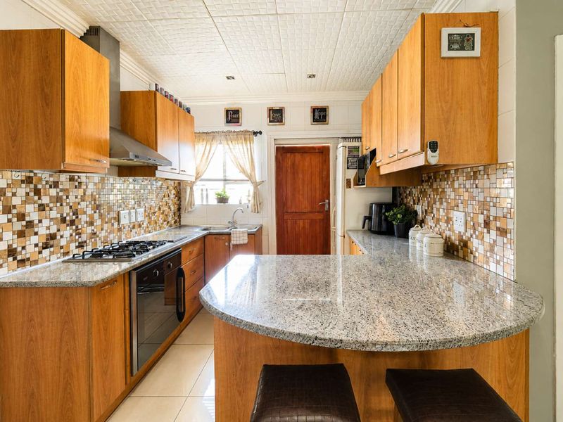 A functional kitchen featuring wooden cabinetry, granite countertops, a gas hob, and a mosaic tile backsplash with a breakfast nook area.
