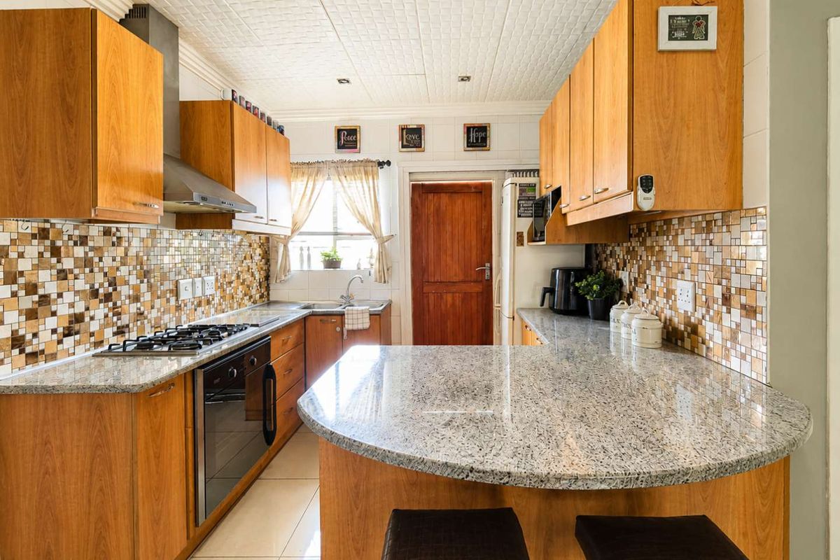 A functional kitchen featuring wooden cabinetry, granite countertops, a gas hob, and a mosaic tile backsplash with a breakfast nook area.