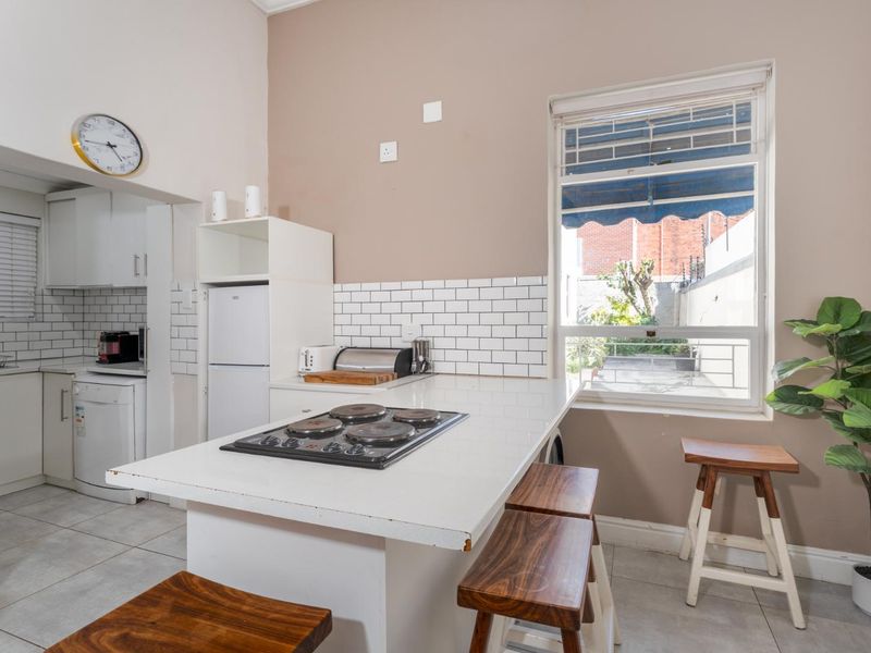 Open-plan kitchen featuring a central island with an integrated electric hob, subway tile backsplash, and tiled flooring, with an adjacent scullery area.