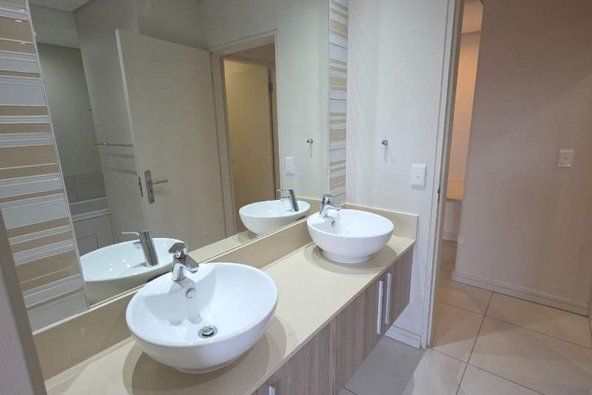 Modern bathroom featuring a double vanity with vessel sinks, stone countertop, wood-finish cabinetry, and a large wall-mounted mirror with recessed downlighting.