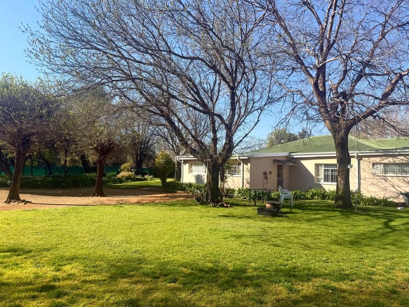 A view of the rear exterior of the farm property, featuring a well-maintained lawn, mature trees, and a single-story building with a metal roof.