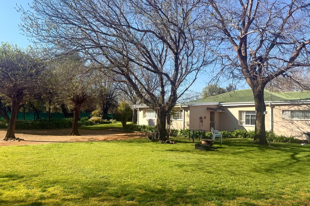 A view of the rear exterior of the farm property, featuring a well-maintained lawn, mature trees, and a single-story building with a metal roof.