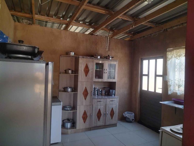 A rustic kitchen area featuring exposed timber roof rafters, tiled floors, and built-in cabinetry, requiring significant finishing work to complete the interior space.