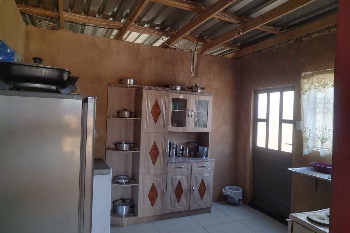 A rustic kitchen area featuring exposed timber roof rafters, tiled floors, and built-in cabinetry, requiring significant finishing work to complete the interior space.