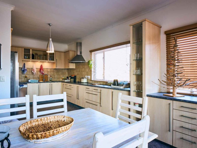 Open plan kitchen and dining area featuring light wood cabinetry, laminate countertops, tiled backsplash, and functional built-in storage with integrated lighting.