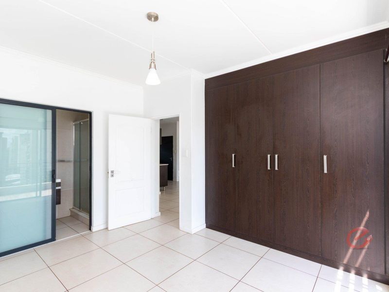 A bright, empty bedroom featuring dark wood built-in cupboards, neutral tiled flooring, and direct access to an en-suite bathroom.