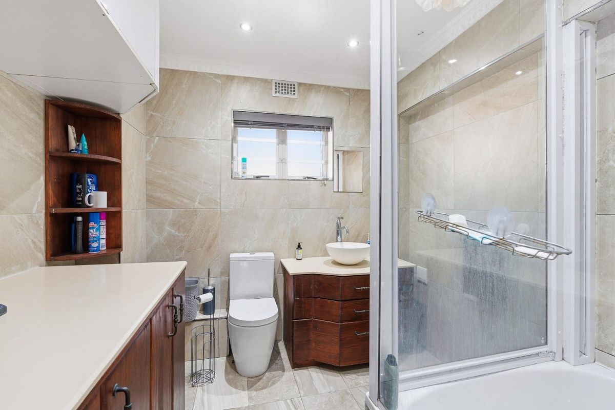 A functional bathroom featuring a vessel sink vanity, toilet, and a glass-enclosed shower with neutral wall and floor tiling.