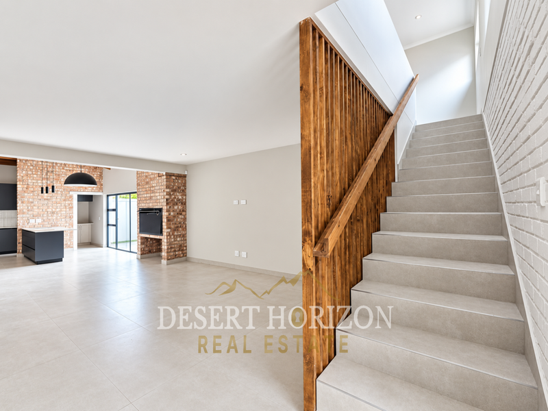 Spacious open-plan living area featuring a modern tiled staircase with timber balustrade, exposed brick accents, and a sleek kitchen island.
