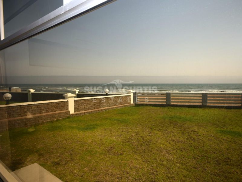A view of the ocean and beach from the property, featuring a landscaped lawn and a brick boundary wall.