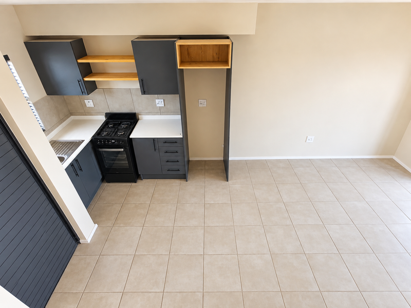 A clean, modern kitchen featuring dark grey cabinetry, a gas stove, oven, and neutral tiled flooring in an open-plan layout.