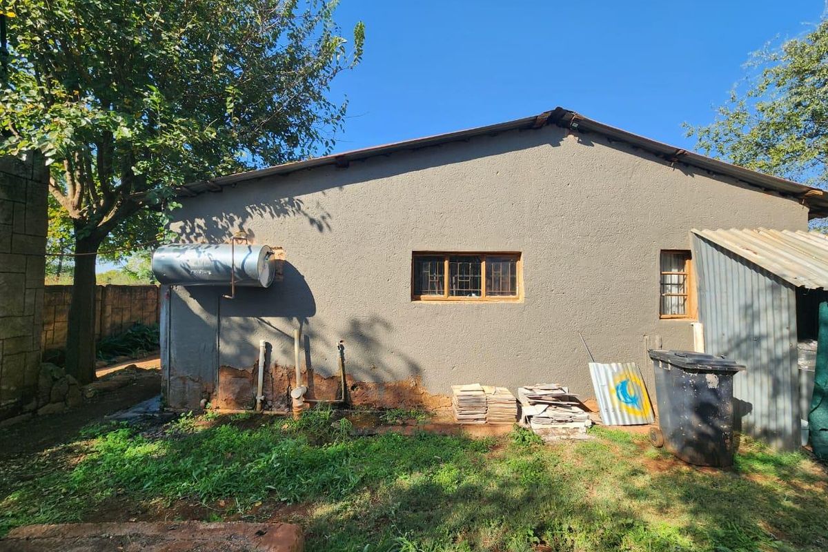 Rear exterior view of the property showing plastered masonry walls, timber frame windows, and an external geyser unit with exposed plumbing.