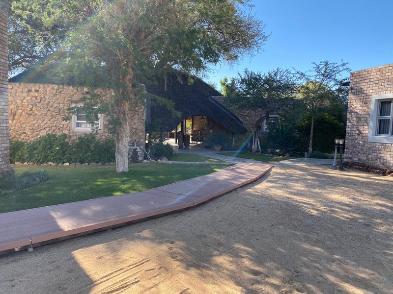 A view of the rear exterior featuring a thatched roof structure, stone and brick masonry, and a wooden walkway leading through the garden.