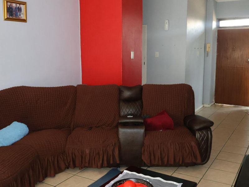 A living room area featuring tiled flooring and a wooden entrance door, with visible wear on the wall surfaces.