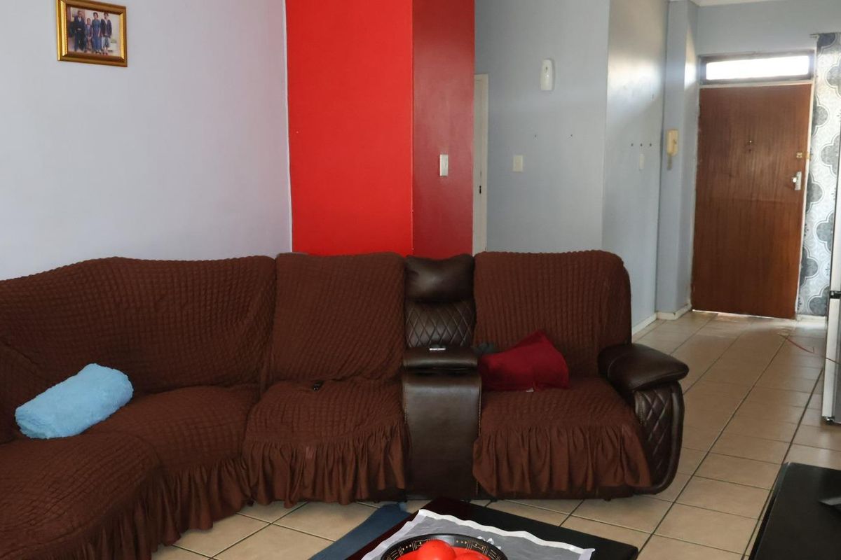 A living room area featuring tiled flooring and a wooden entrance door, with visible wear on the wall surfaces.