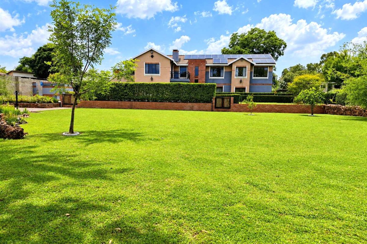 A spacious rear garden featuring a well-maintained lawn, mature hedging, and a view of the multi-story residential building with installed solar panels.