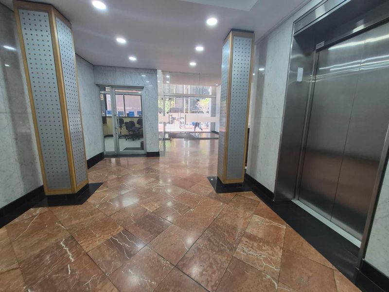 A professional office building lobby featuring polished marble flooring, stainless steel elevator access, and modern recessed lighting with glass entrance doors.