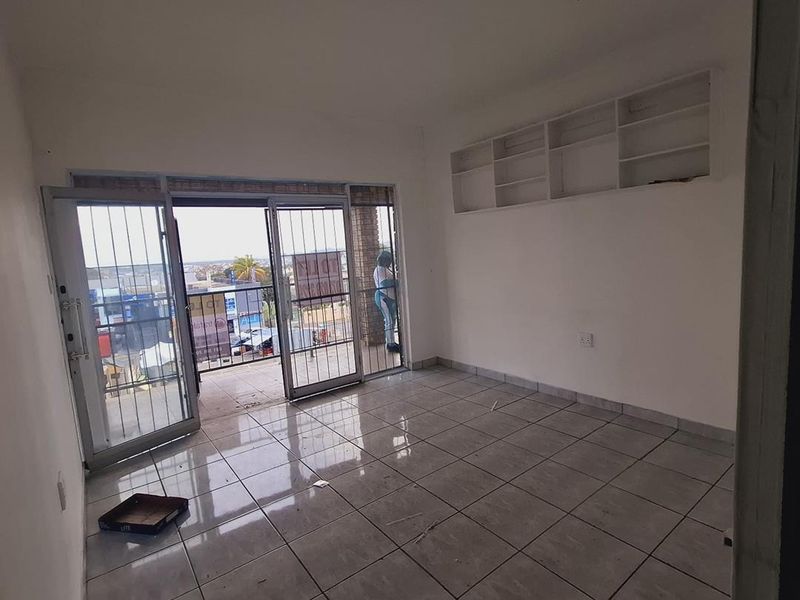 An empty living area featuring tiled flooring, built-in wall shelving, and sliding glass doors leading to a balcony with security gates.