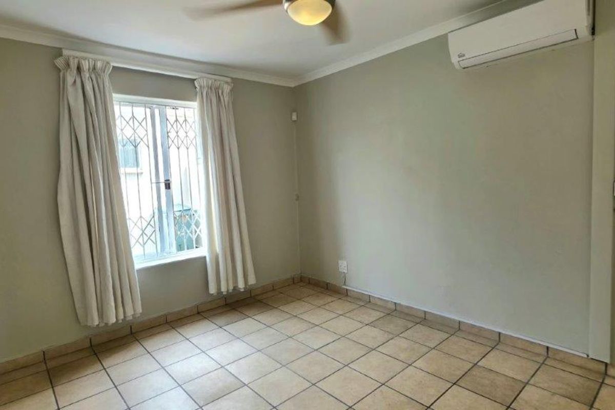 A bright, empty bedroom featuring ceramic tile flooring, a ceiling fan, and a wall-mounted split-system air conditioner.