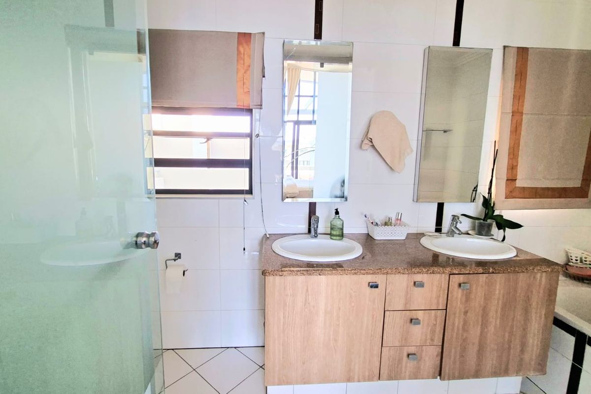 A functional bathroom featuring a double vanity with granite countertop, dual sinks, wall-mounted mirrors, and a glass-enclosed shower area.