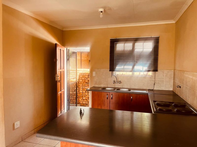 A functional kitchen featuring built-in cabinetry, laminate countertops, an electric hob, and a double sink, with direct access to an exterior security gate.